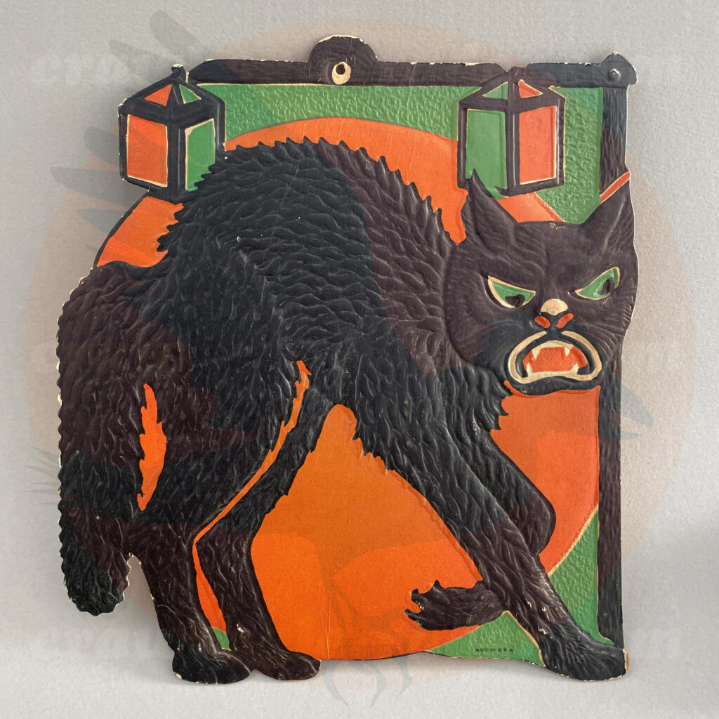 Black cat sneaking under the moon with green/orange lanterns hanging from a post - a Beistle embossed diecut paper vintage Halloween collectible offered by trade/buy/sell Craw-Bogle Trader collector, a companion site to The Halloween Retrospect archive library.