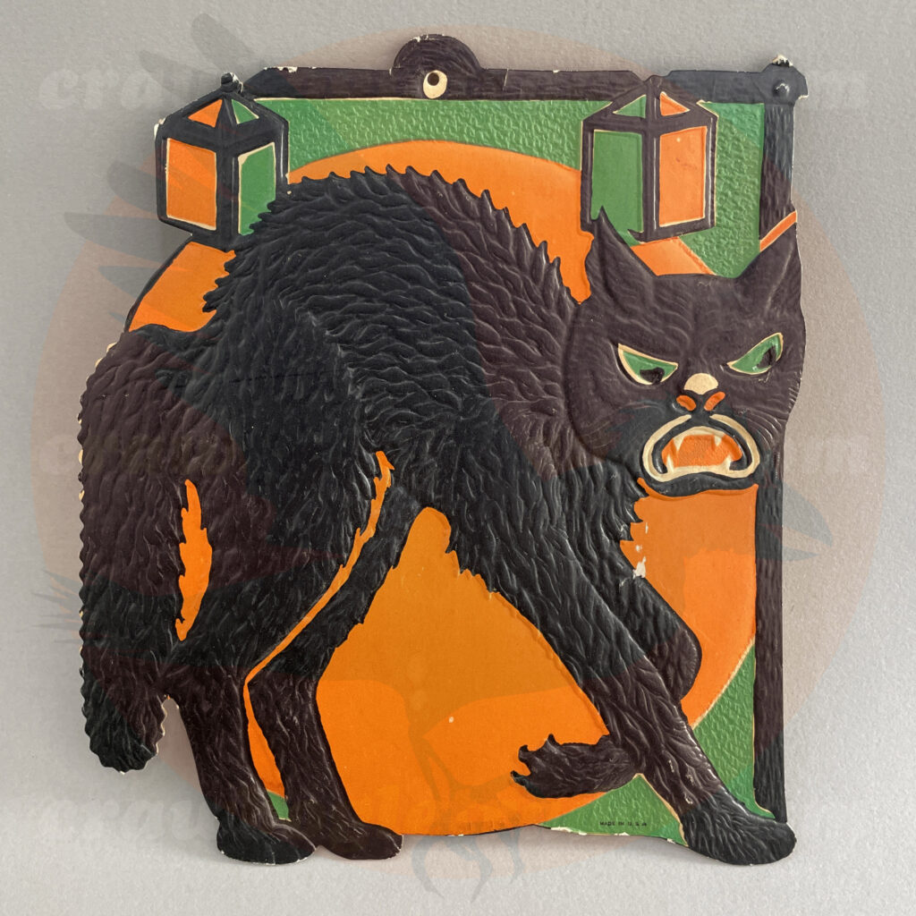 Black cat sneaking under the moon with green/orange lanterns hanging from a post - a Beistle embossed diecut paper vintage Halloween collectible offered by trade/buy/sell Craw-Bogle Trader collector, a companion site to The Halloween Retrospect archive library.